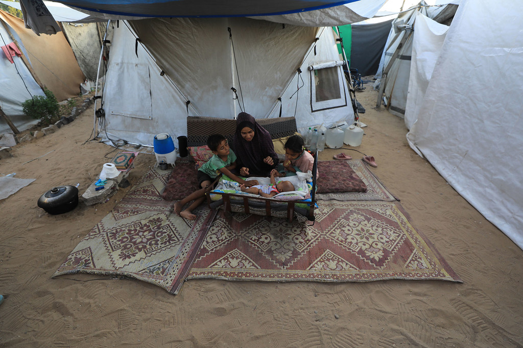 Una mujer sentada con sus tres hijos en un campo de desplazados del oeste de Gaza; su bebé sólo tiene dos meses.